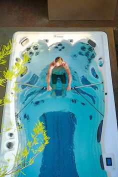 a man is swimming in a hot tub with blue water and green plants around him