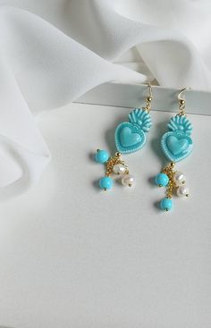 Sicilian earrings made of: - Sicily Ceramic sacred hearts (24 mm x 15 mm), light blue color; - Smooth stones (4 mm), turquoise color; - Freshwater pearls (4 mm), white color, - 925 open hooks. Lenght : 6 cm / 2,36 inches * SHIPPING * Your order will be shipped within 1-3 business days from your purchase. You can choose between 2 shipping methods: STANDARD MAIL (NOT TRACEABLE) It is a cheap and fast shipping method, but NOT TRACEABLE. Chapeau Atelier is not responsible for any postal disruptions, Light Blue Heart Beads Jewelry For Gift, Light Blue Heart Beads Jewelry Gift, Turquoise Heart Beads Dangle Earrings, Turquoise Dangle Earrings With Heart Beads, Blue Dangle Heart Pierced Earrings, Sacred Hearts, Polymer Earrings, Baroque Fashion, Light Blue Color