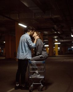 a man and woman kissing while sitting in a shopping cart inside an empty parking garage