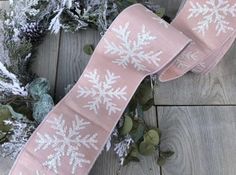 a pink ribbon with white snowflakes on it sitting next to some evergreen branches