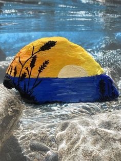 a painted rock sitting on top of a sandy beach next to the ocean under water