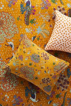 three pillows sitting on top of a bed covered in yellow and white floral print fabric