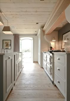 a long narrow kitchen with white cabinets and wood flooring, along with an open door leading to the outside