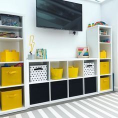 there is a television mounted on the wall above some shelves with bins and baskets