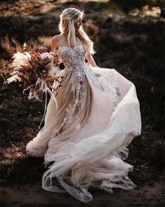 a woman in a wedding dress is walking through the grass with her hair pulled back