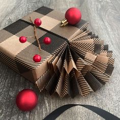 an ornament wrapped in brown and black paper with red balls on it next to a ribbon