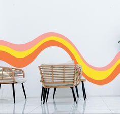 two wicker chairs sitting next to each other in front of a wall with an orange and yellow wave painted on it