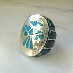 This is a vintage Navajo Native American thunderbird mens turquoise ring.  The ring is heavy sterling silver.  The sides of the band are set with green & blue turquoise stones. There is some deep matrix on these side stones that should not be mistaken for cracks. The bright blue turquoise inlay in the thunderbird is flush.  The ring face measures 1 3/16" long x 15/16" wide.  The band is sized at a 9 1/2.  Total weight of the ring is 27.1 grams.   This is a vintage, previously owned ring.  Therefore, light wear can be expected.  There is no visible damage. Vintage Turquoise Ring With Polished Finish For Anniversary, Southwestern Polished Turquoise Ring Collectible, Vintage Sterling Silver Turquoise Ring With Polished Finish, Vintage Sterling Silver Turquoise Ring With Inlay, Antique Silver Turquoise Ring With Patina, Vintage Silver Turquoise Ring With Polished Finish, Vintage Turquoise Ring With Polished Finish, Artisan Silver Turquoise Ring With Inlay, Collectible Vintage Turquoise Ring With Polished Finish