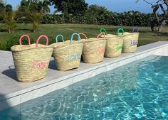 four large baskets sitting on the edge of a swimming pool with handles painted in different colors