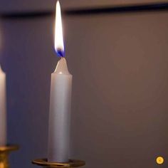 two white candles with one lit and the other on a gold plated candle holder