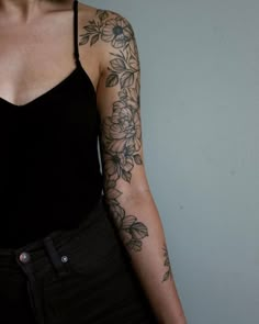 a woman with tattoos on her arm and shoulder standing in front of a white wall