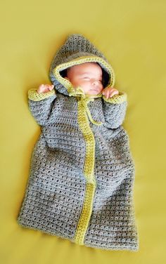 a crocheted baby is wrapped up in a gray and yellow blanket on a yellow background