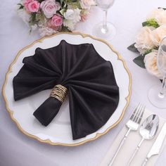 a white plate topped with black napkins next to silverware and flowers on top of a table