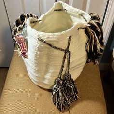 a white basket sitting on top of a wooden floor next to a door with two tassels hanging from it