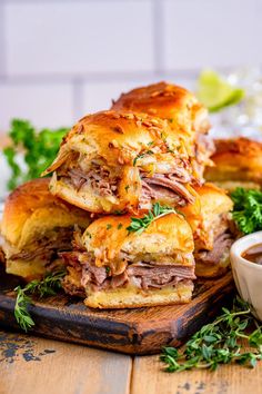 a pile of sandwiches sitting on top of a wooden cutting board next to a bowl of dipping sauce