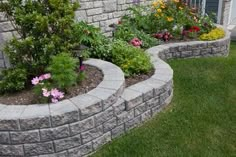 some flowers and plants are growing in the corner of a brick garden wall, along with another flower bed