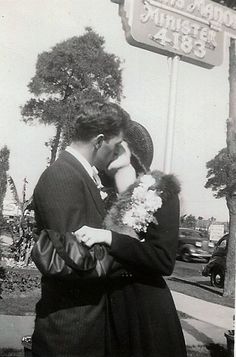 an old black and white photo of a man talking on a cell phone in front of a street sign