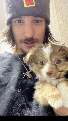 a man holding a small dog wearing a beanie and looking at the camera with an intense look on his face