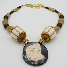 This 1 of a kind necklace features alovely handmade ceramic Geisha pendant made by an American artist.  Pendant is about 2 inches in height x 1 3/4 inch in width. Back of pendant is finished with black and cream splotched/swirled pattern.  Pendant hangs from necklace made with fancy brass beadcaps, large handmade vintage brass and resin focal beads from Nepal, very nice handmade brass beads fro Nigeria,  These beads were shaped entirely by hand using hammer...I love the way they show hammer marks.  I have also used 4 Mongolian Jet beads and tiny black glass beads. Necklace fastens with my signature large fancy brass clasp and very nice textured goldplated chain. Length adjusts from about 19 - 21 inches. Artistic Handmade Jewelry With Round Beads, Handmade Artistic Jewelry With Round Beads, Artistic Beaded Necklaces As Gift, Artistic Handmade Round Bead Jewelry, Artistic Beaded Necklace For Gifts, Artistic Beaded Necklace Gift With Round Beads, Artistic Beaded Necklace For Gift, Artistic Beaded Necklaces For Gifts, Artistic Round Beads Necklace For Gift