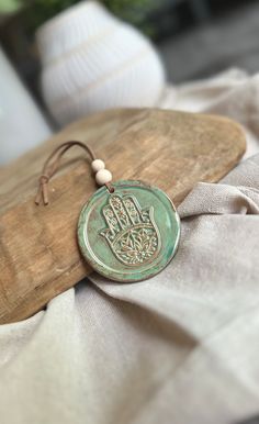 a wooden board with a green ceramic hamsa hanging from it's side on top of a white cloth