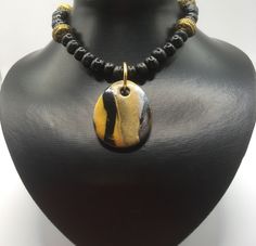 I've used the Japanese  technique mokume gane to create this polymer clay pendant. It comprises gold, white and black polymer clay. The pendant has been teamed with black wooden beads and golden spacer beads. The necklace is closed with a lobster claw lock and extends to 48cm if using the extender chain. The pendant measures 4.2 x 3.5cm. For more jewellery in similar colours, see the polymer clay section. Artisan Gold Custom Necklace Pendant, Artisan Gold Pendant Custom Necklace, Artisan Gold Custom Pendant Necklace, Gold Carved Round Pendant Necklace, Handmade Gold Necklace With Rectangular Pendant, Gold Handmade Necklace With Rectangular Pendant, Unique Gold Polymer Clay Jewelry, Spiritual Polymer Clay Pendant Necklace, Spiritual Polymer Clay Necklaces For Gifts