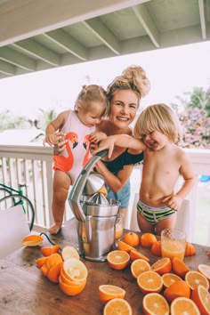 two children and an adult are standing in front of a table full of oranges