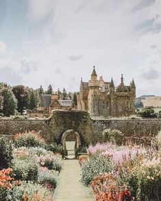 an old castle surrounded by lots of flowers and greenery with a path leading to the entrance