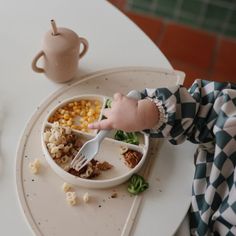 a small child is eating food from a bowl on a tray with a fork and spoon