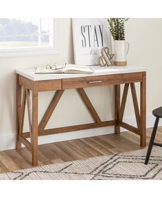 a wooden desk with a book and glasses on it next to a chair in front of a window