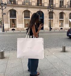 a woman looking at her cell phone while standing on the sidewalk in front of a building