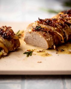 sliced meat on a cutting board with herbs and seasoning sprinkled around it