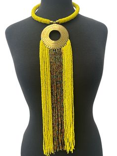 This stunning necklace brings together the beauty of African culture with elegance. The brass pendant features intricate engraving and a long fringe of yellow beaded strands, creating a unique and eye-catching piece. The necklace is perfect for any occasion and will add a touch of sophistication to any outfit. The beaded strands are crafted from high-quality materials, ensuring durability and longevity. This necklace is a must-have for anyone who loves African art and jewellery. Material: Beads and decorative brass metal. Fringe - 40cm Neck Width - 50cm Colour: Yellow, Gold, Multicolour Weight: 200g Traditional Beaded Fringe Necklace, Bohemian Gold Lariat Necklace With Dangling Beads, Gold Beaded Long Necklace For Festival, Gold Bohemian Lariat Necklace With Dangling Beads, Gold Jewelry With Beaded Fringe For Festival, Adjustable Yellow Lariat Necklace, Gold Beaded Chain Necklace For Festival, Traditional Adjustable Beaded Fringe Necklaces, Traditional Adjustable Beaded Fringe Necklace