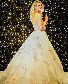 a woman in a white dress standing next to a wall covered with stars and lights