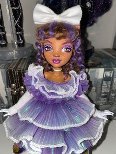 the doll is wearing a purple dress and white headband with big blue eyes,