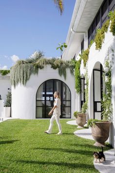 a woman walking across a lush green field next to a white building with lots of windows