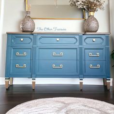 a blue dresser with two vases on top and a mirror above it in a room