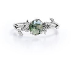 a ring with an oval green stone surrounded by leaves and diamonds on the band, set in white gold