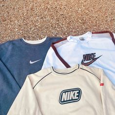 three nike sweatshirts laying on the ground next to each other and one is white