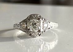 an old - fashioned diamond ring sits on a white countertop, with the center stone partially surrounded by filigrees