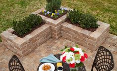 an outdoor table with flowers and plates of food on it next to brick planters