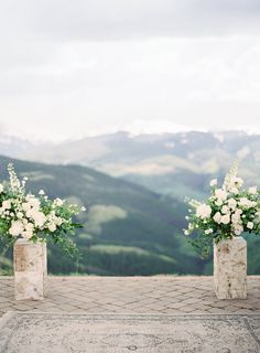 two vases filled with white flowers sitting on top of a stone slab covered ground