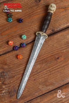 a large knife sitting on top of a wooden table next to dices and beads