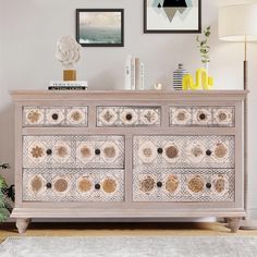 a white dresser sitting in a living room next to a wall with pictures on it