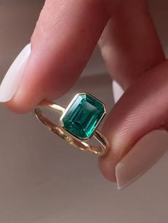 a woman's hand holding a ring with an emerald stone in the middle of it