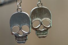 two silver skull shaped earrings hanging from chains