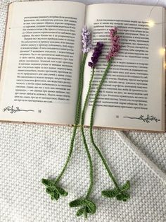 two crocheted flowers laying on top of an open book with string lights in the background