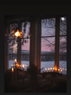 candles are lit in front of a window overlooking the snow covered ground and trees outside