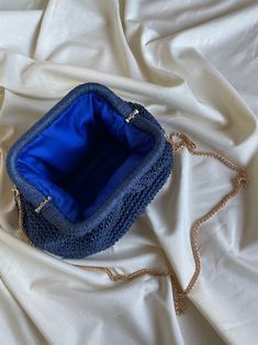 a blue purse sitting on top of a white cloth covered bed with a gold chain