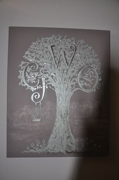 a white tree with the letter w hanging from it's trunk in front of a gray wall