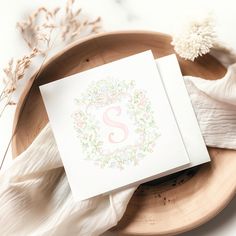 a card with the letter s on it sitting on top of a wooden plate next to dried flowers